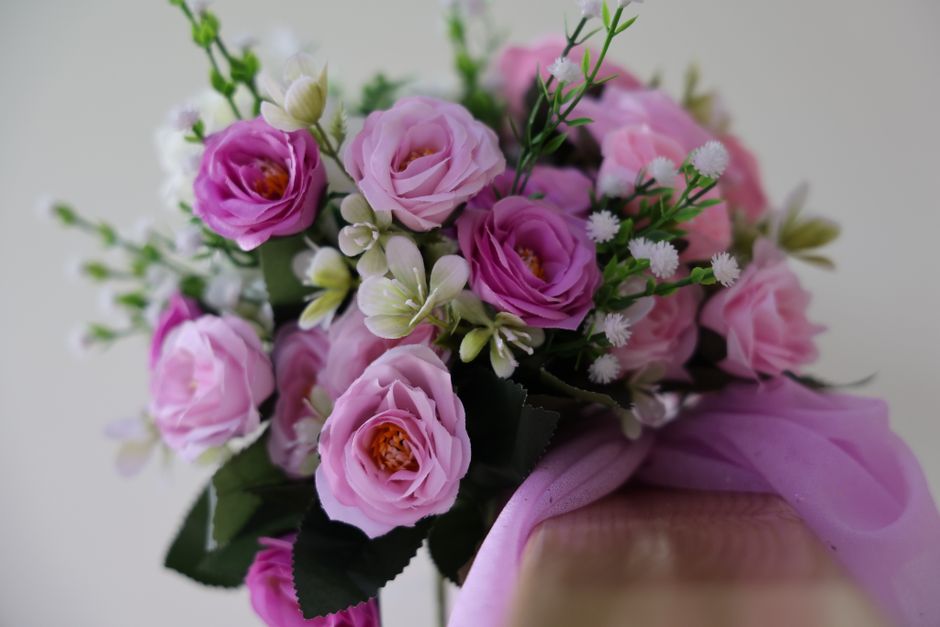 A close-up image of a floral bouquet arranged with pink lisianthus, white freesias, and small white daisy-like flowers, complemented by green foliage. The bouquet is wrapped in soft pink tissue paper 