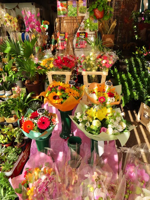 A display of colorful floral bouquets arranged in various-sized vases and wrapping, prominently featuring bright sunflowers, pink gerbera daisies, and white chrysanthemums. The bouquets are set on a p