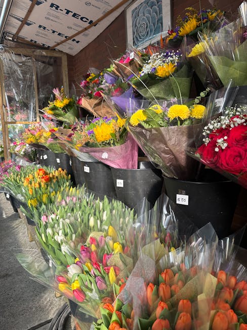 A display of multiple bouquets of fresh flowers arranged in black buckets inside a flower shop. The bouquets feature a variety of colorful blooms including yellow chrysanthemums, purple irises, pink t