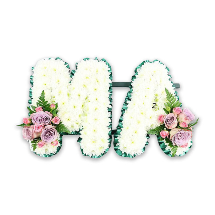 This image shows an elegant funeral letter tribute spelling the word MA, created as a personalised homage to a mother or mama with strong ties to Petts Wood. The two capital letters stand side by side, joined discreetly at the back so they appear as one continuous piece, rather like a single, heartfelt message. Every visible surface of the letters is blanketed with crisp white chrysanthemums, their small daisy-like heads densely arranged to form a uniform, velvety layer. The blooms have that just-opened freshness you might notice when passing a florist near Petts Wood station first thing in the morning, with no wilting or discolouration, only clean white petals radiating from soft green centres. Around the perimeter of both letters runs a firm emerald green ribbon, gently gathered into pleats. This ribbon edge frames the chrysanthemums sharply, providing structure and definition while adding a rich, jewel-like green accent that echoes the wooded feel of the local area. At the foot of the M, a compact spray of flowers in pastel pink and lilac tones brings a note of tenderness, mirrored symmetrically at the base of the A. In each spray, larger roses in soft lavender and soft blush unfold among smaller pink spray roses, creating layers of texture and shade. A single fern frond extends gracefully from each cluster, its feathery leaflets lending a natural softness and movement. The arrangement is photographed on a plain white background, free of distractions, accentuating the careful craftsmanship and balanced proportions. This MA funeral tribute feels calm, respectful, and intimate, the sort of bespoke piece that might accompany a final farewell for a beloved mum at a local Petts Wood service or crematorium.