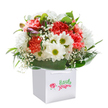 A sense of effortless joy flows from this vibrant bouquet, beautifully arranged by Petts Wood florists and presented in a striking white gift bag with flowing ribbon handles. Set against a flawless white background, the composition combines the pillowy softness of coral and rich red carnations with the clean, lighthearted charm of white daisies crowned by green-gold centers. Wisps of delicate baby's breath add their airy, cloud-like texture, creating an inviting sense of innocence and celebration. Hidden among the foliage, unopened buds tinged with purple suggest the quiet anticipation of springtime walks through Petts Wood's shaded avenues. Encasing the floral display, broad, glossy dark-green leaves fan out, providing both support and a luxurious finish that evokes the well-kept gardens of the area. The entire arrangement, artfully crafted into a full and rounded shape, sits proudly in its pristine bag, a symbol of ready-to-give delight-be it to mark a meaningful birthday, say thank you, or simply deliver a spontaneous smile to someone in the heart of Petts Wood. The bouquet's freshness, subtle fragrance, and careful balance of colour and texture all come together to create an uplifting gesture, one that truly reflects the joy and thoughtfulness inherent in local Petts Wood flower delivery.